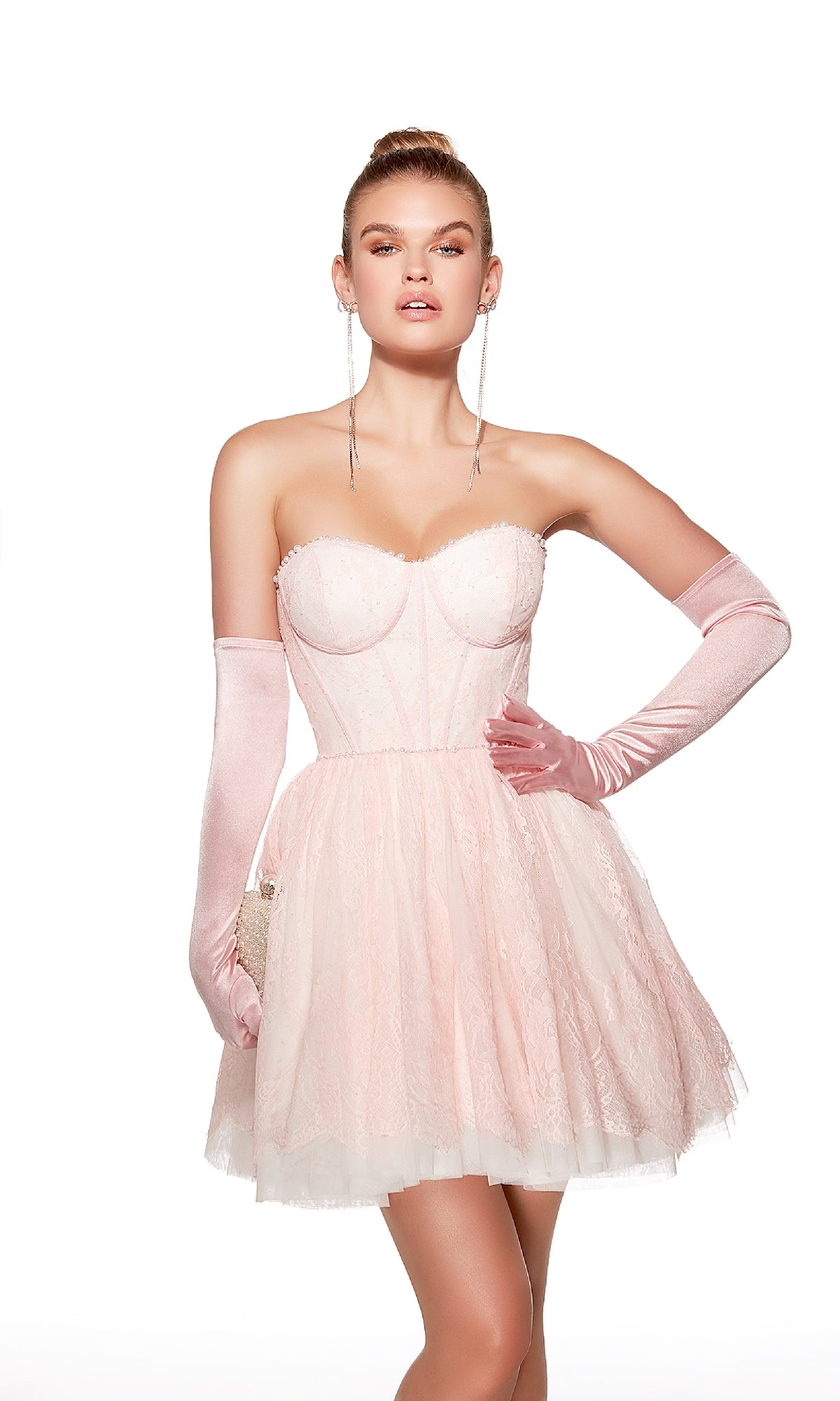 A woman stands against a white background wearing the Alyce 30041 Strapless Short Lace Hoco Dress, a pale pink cocktail dress with a corset bodice, tulle skirt, and long matching gloves.